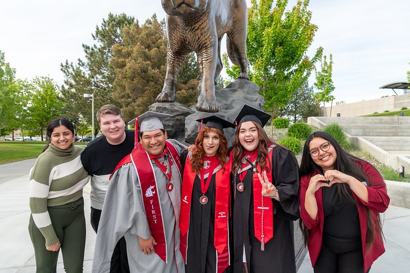 Students in regalia posing for a photo in front of a Coug statue