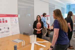 Student speaking with a judge in front of their research poster and a model of an SMR reactor on the table.