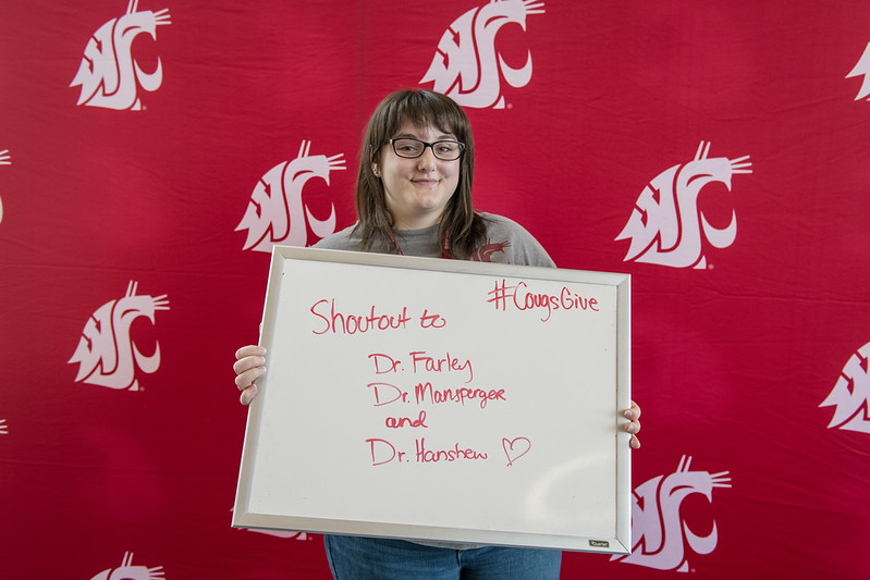 Student holds a whiteboard in front of a crimson background