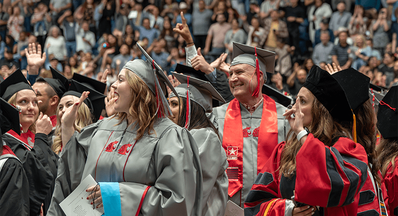 Students in graduation regalia waving to their families in the Toyota Center