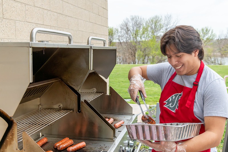 Student in a crimson Coug apron grilling hot dogs