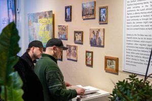 Guests at the Eastside Temporalities exhibit reading a book in front of a wall of framed photos.
