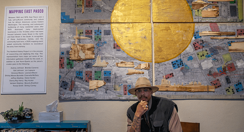 Artist Joel Nunn-Sparks seated in front of a large abstract map of East Pasco.