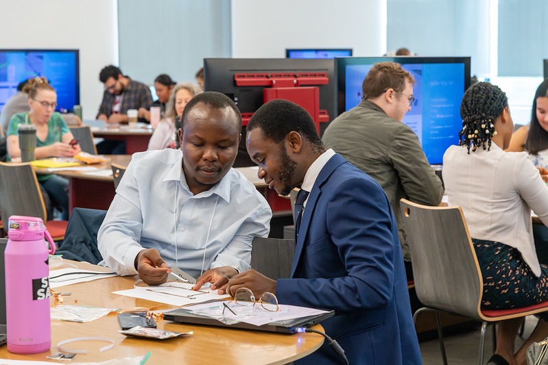 Two men seated at a table in a classroom connecting a circuit together.