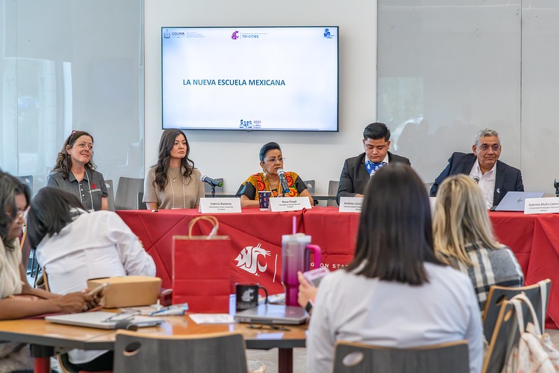 Five people seated at a table with microphones and a screen behind them that reads, La nueva escuela mexicana.