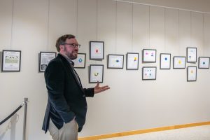 Ethan Smith gesturing to a row of framed pieces of art on a gallery wall.