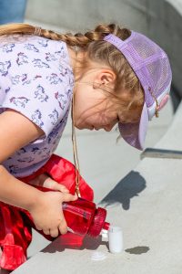 Child pouring water from a WSU water bottle into a small plastic container.