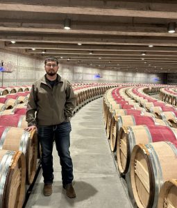 Hector Estrada standing among wine barrels