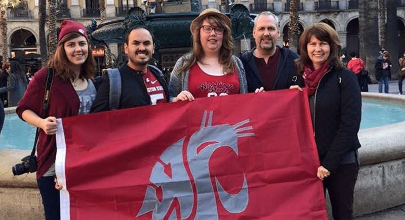 Five members of the Ohl family holding a crimson WSU Coug flag in front of a water fountain.