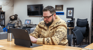 Jeff Wilson sits with a tablet computer, conversing with a student across the desk table.