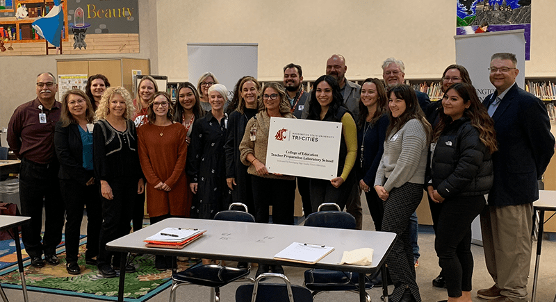 Teachers from Maya Angelou Elementary and leadership from WSU Tri-Cities, and the Pasco School District stand with the sign identifying Maya Angelou Elementary as a WSU Tri-Cities College of Education Laboratory School.