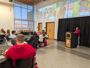 Peer Mentor Alyssa Perez speaking behind a podium to a seated audience.