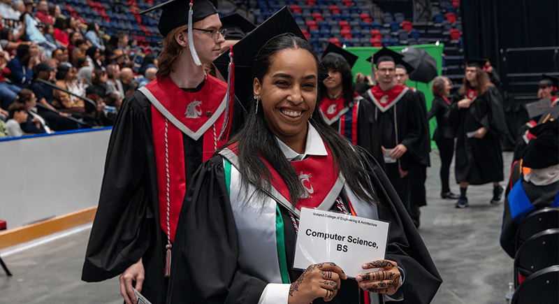 Reem Osman at Commencement wearing regalia and holding a sign that says Voiland College of Engineering & Architecture Computer Science, BS