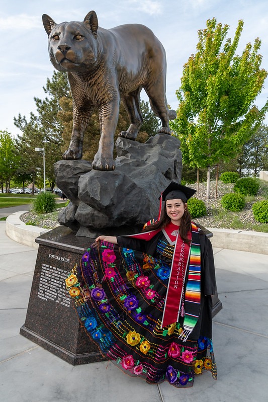 Student Tania Castellano standing in front of a bronze Coug statue wearing graduation regalia.