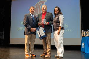 John Mancinelli being presented an award on stage while holding a Kennewick School District tote bag.