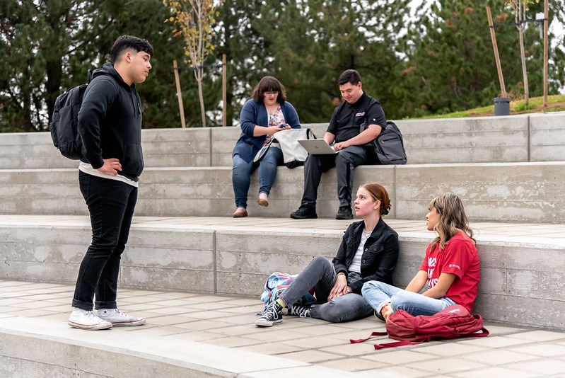 Five students with backpacks using the WSU Tri-Cities amphitheater seating. One is standing.