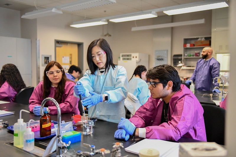 WSU Tri-Cities professor putting liquid into a beaker while two students seated on either side watch.