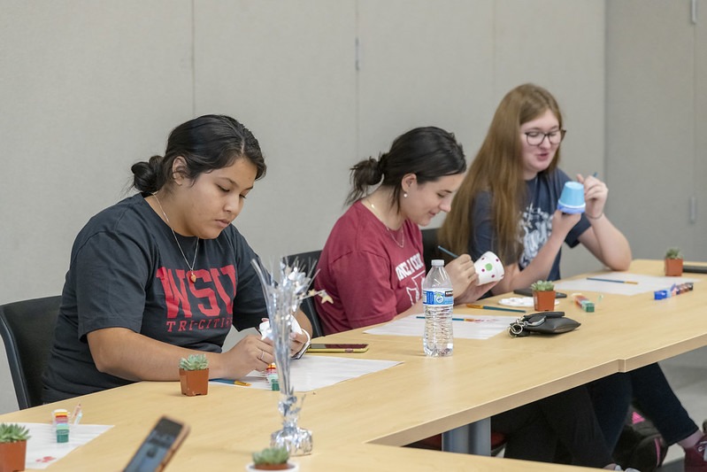 Three students sitting at a table painting mini plant pots.