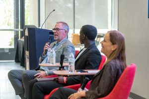 H2C President Ken Langdon speaks into a microphone while ASWSUTC President Romeo Ross and Executive Vice President Sandra Haynes sit next to him.