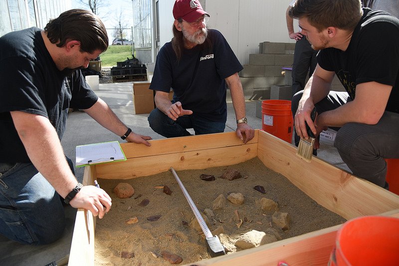 Students and professor excavating artifacts out of a wooden box.