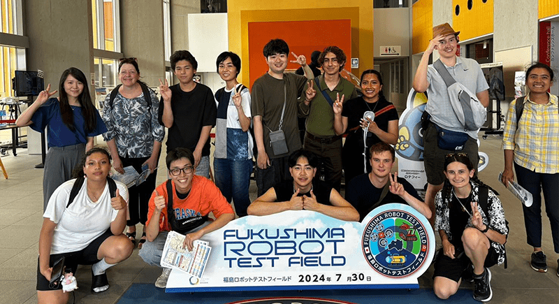 WSU Tri-Cities students and Japanese students posing for a photo in front of a sign that reads "Fukushima Robot Test Field".