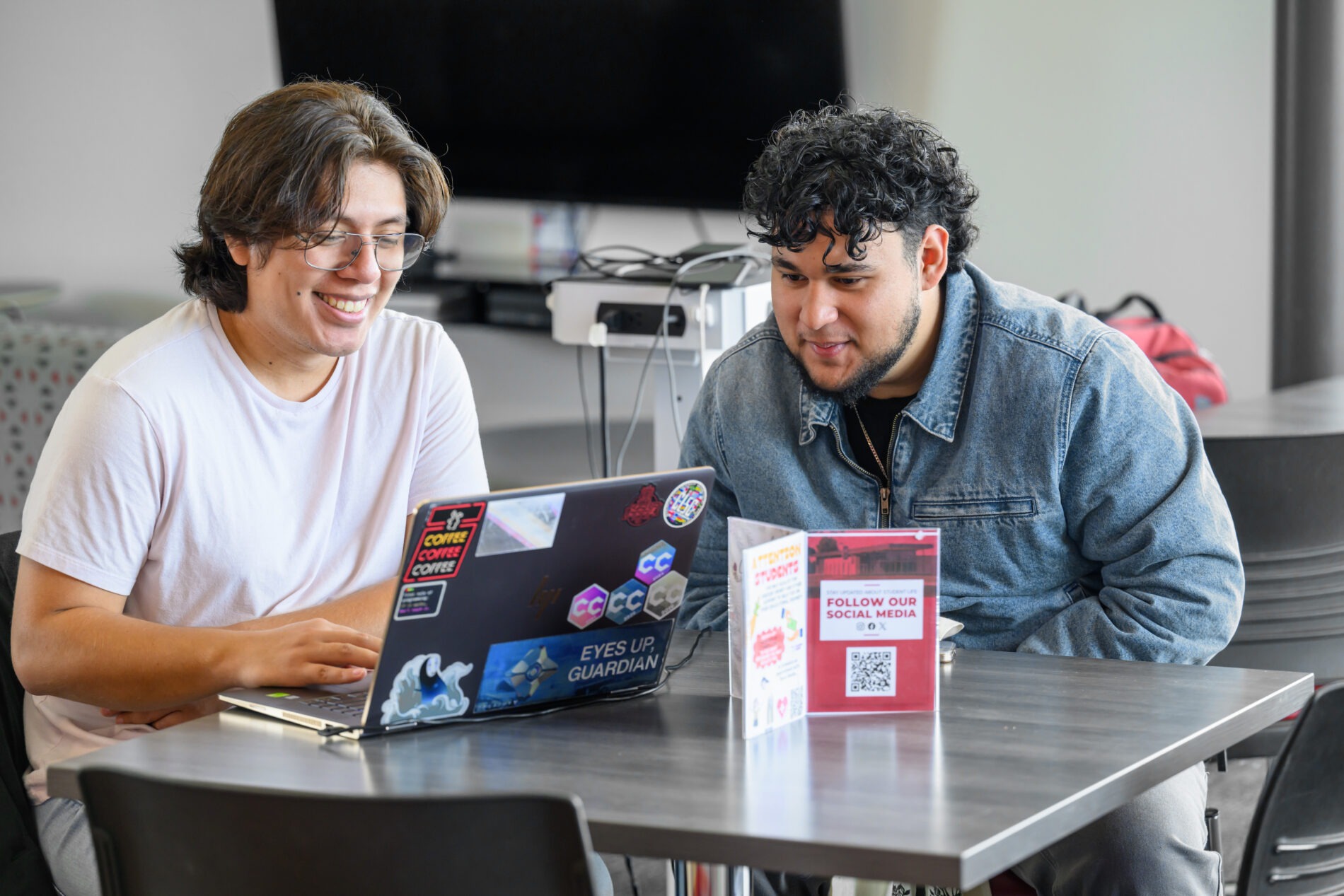 Two students seated at a table looking at a laptop.