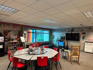 Room with a large table, chairs, a TV, arcade machine, and flags lining the walls.