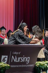 Edith Nateras hugging her daughter on stage in front of a WSU College of Nursing banner.