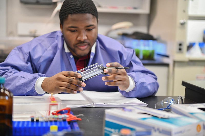 Student in a lab coat holding a piece of science equipment.