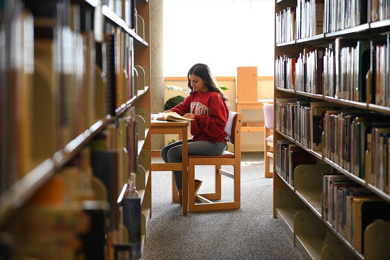 Student wearing a crimson WSU sweater reading a book in the library.