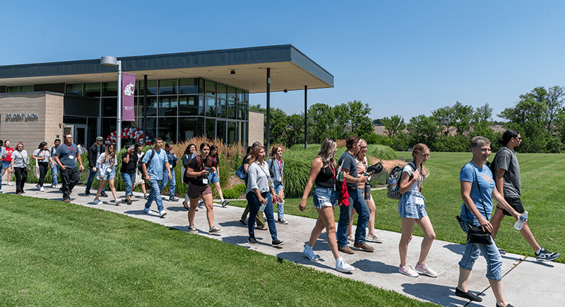 Group of students and their families walking on a path in front of the Student Union Building on the WSU Tri-Cities campus.