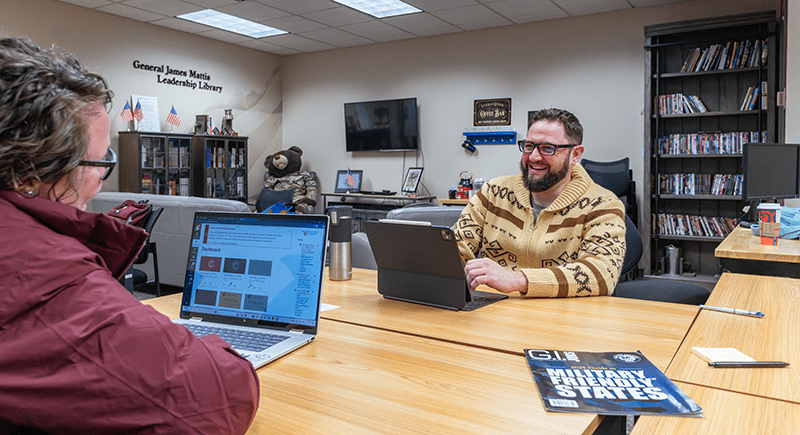 Jeff Wilson sits with a tablet computer, conversing with a student across the desk table.