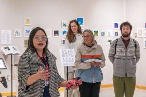Yichien Cooper speaks to an audience standing in an art gallery.