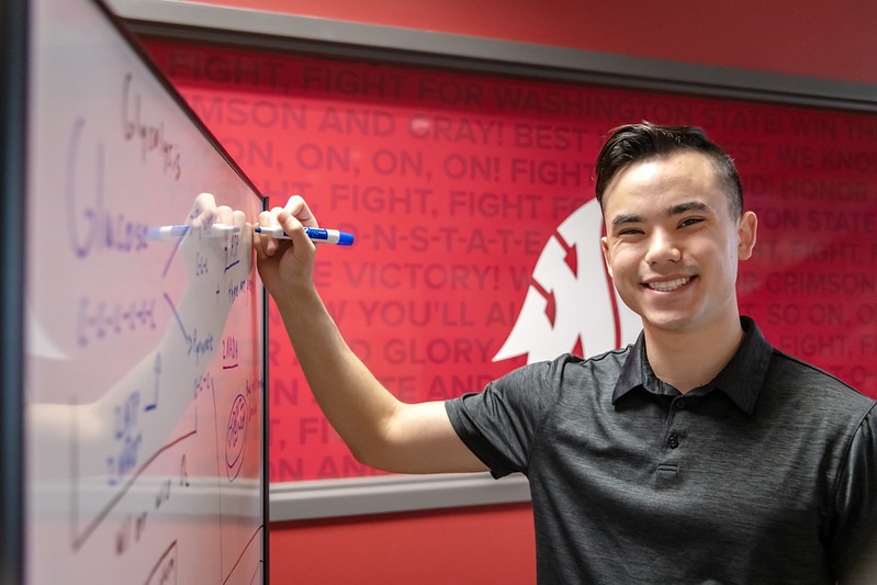 Student Zarryn Duong writing on a whiteboard in front of a Coug backdrop.