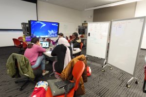 Coding Cougs students sitting around a table planning their project. To he right, two whiteboards are filled with notes.